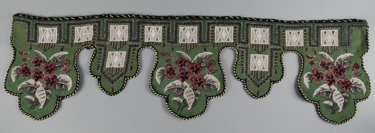 Hyllfrans, lambrequin, grön yllebotten av korsstygn med mönster av korsstygn och pärlor i rött, vitt, svart, grått och ofärgat glas. Kantad med svart och gul snodd av silke och sammet.

