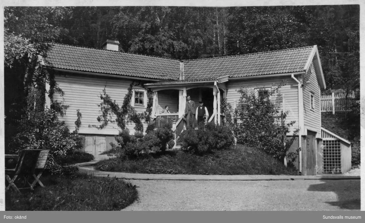 Sven Johan Magnusson på förstukvisten till gårdshuset till Villa Humlegården, Baldersvägen 20 i Stadsbacken. Sven Johan Magnusson arbetade som gårdskarl på Villa Humlegården, som ägdes av Nils Albin Rönnholm, rektor på Läroverket. Han ansvarade bl a för trädgården, husets skötsel och fungerade även som chaufför. Två av barnen Gustav (f. 1896) och Gertrud (f. 1903) ses på bild 1. Bild 2 är tagen 1918. På bild 3 ses Magnusson stå framför Villa Humlegården. Bild 4 visar paret Magnusson framför Villa Humlegården på väg till kolonistugan i föreningen Arbetsglädjen 1921.