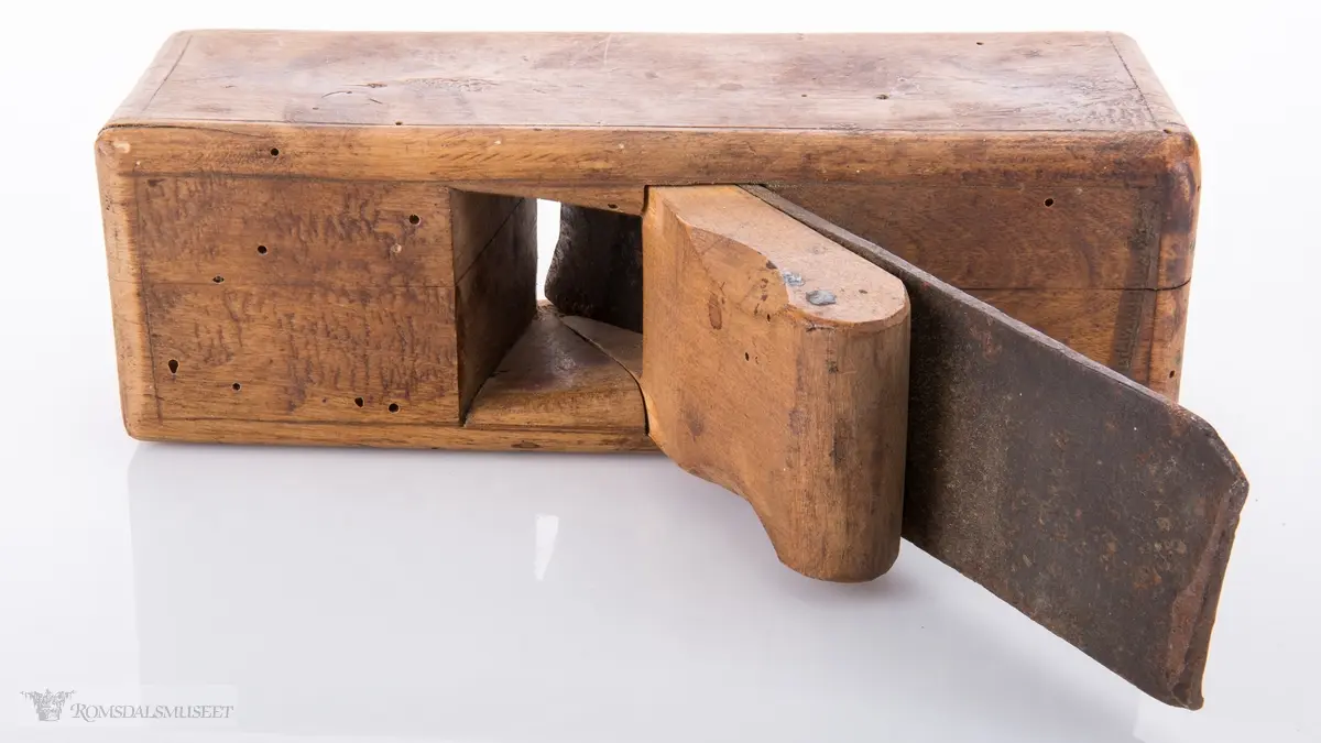 Liten rektangulær høvel med jern og kile. Konkavt u- formet spor i sålen.