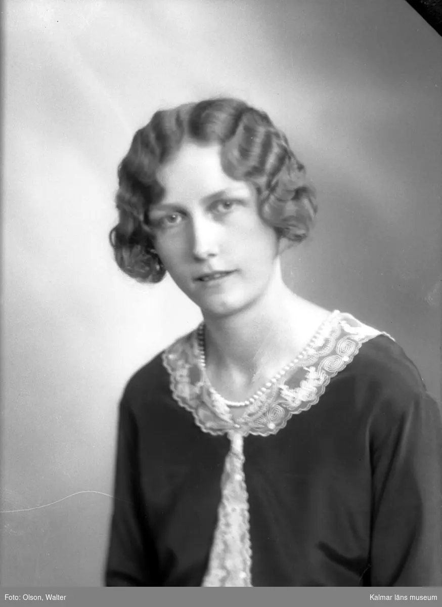 Ateljébild på en kvinna i halsband och spetskrage. Enligt Walter Olsons journal är bilden beställd av Ingrid Wennberg.