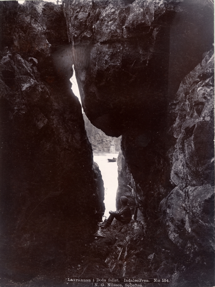 Pojke sittande i spricka i berget. Laxränna vid Döda fallet, Indalsälven, 1899.