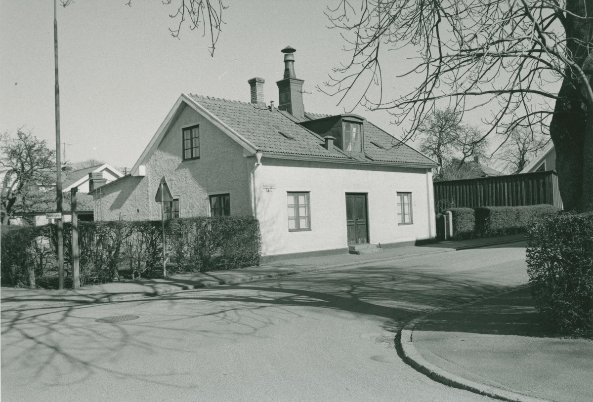 Ett bostadshus med putsad fasad och en häck på Baggensgatan 1 i Ängö.