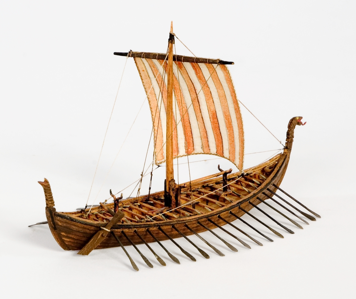 Fartygsmodell, vattenlinjemodell, hel i block av trä, vikingaskepp ("Osebergsskeppet") 800-t. Klinkbyggd, brunt skrov med höga stävar. Riggad med 1 mast, vit- och rödrandigt råsegel. I förstäven drakhuvud. Utrustad med 17 par åror samt styråra (sidoroder).Föremålets form: Vattenlinjemodell