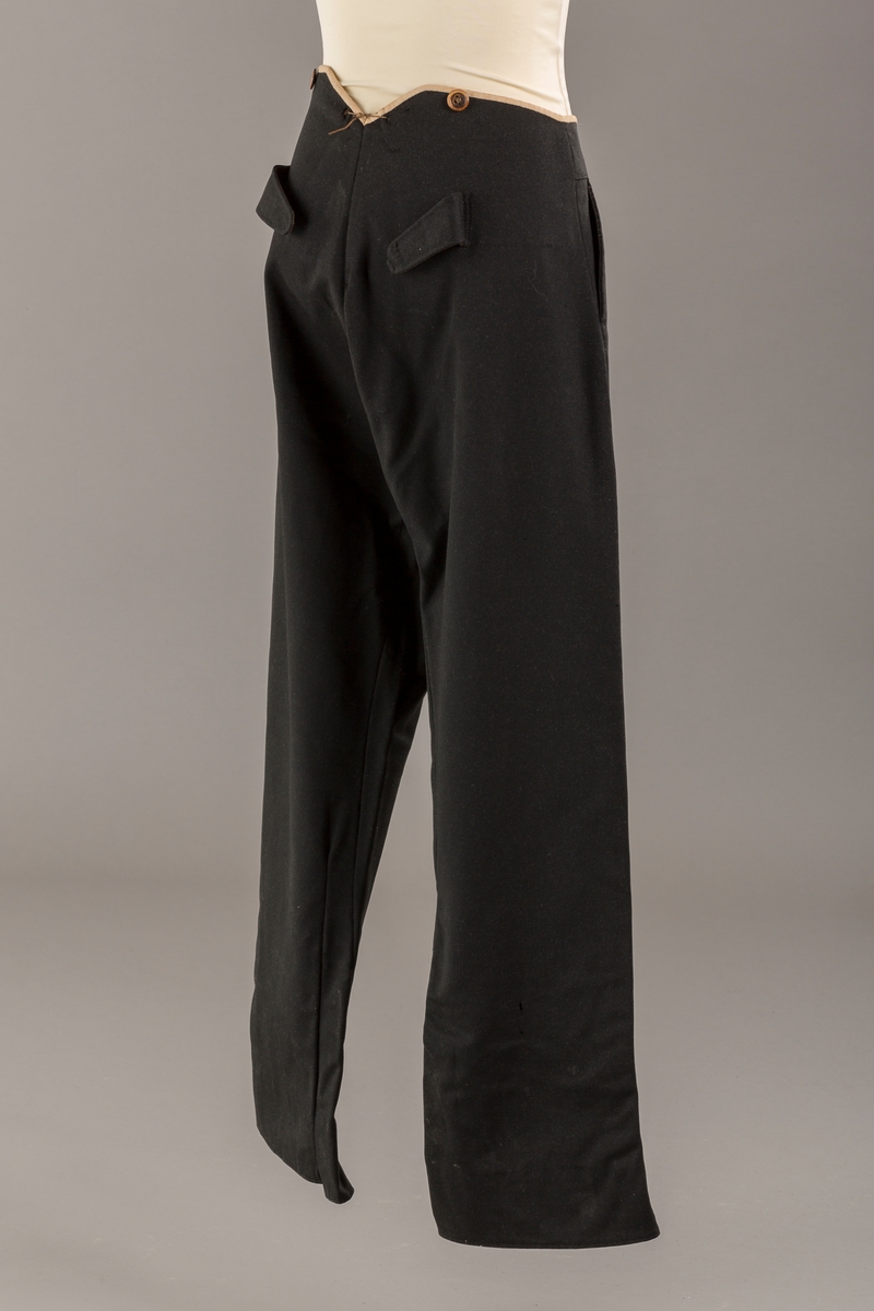 Form: Bena utvidet nederst. Lerretskant rundt livet, spensel i ryggen, mangler spenne i sepnsel?
Delvis foret. To lommer. 5 knapper, mangler en knapp.