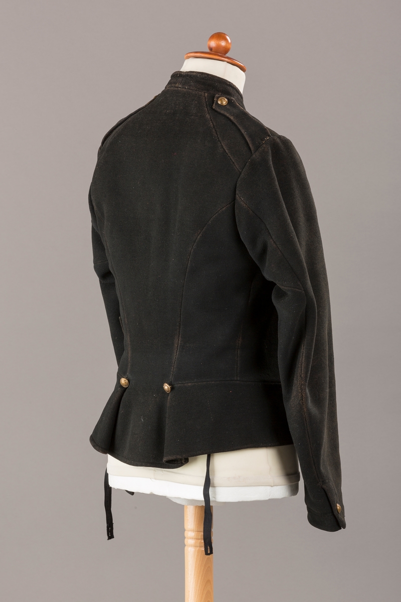 Form: Enkeltspent.

Foret med lin. Forsterket med silke på et lite stykke på ryggen. 12 messingknapper med mønster og tallet 1. Hempe i lin. Bendelbånd med knappehull.