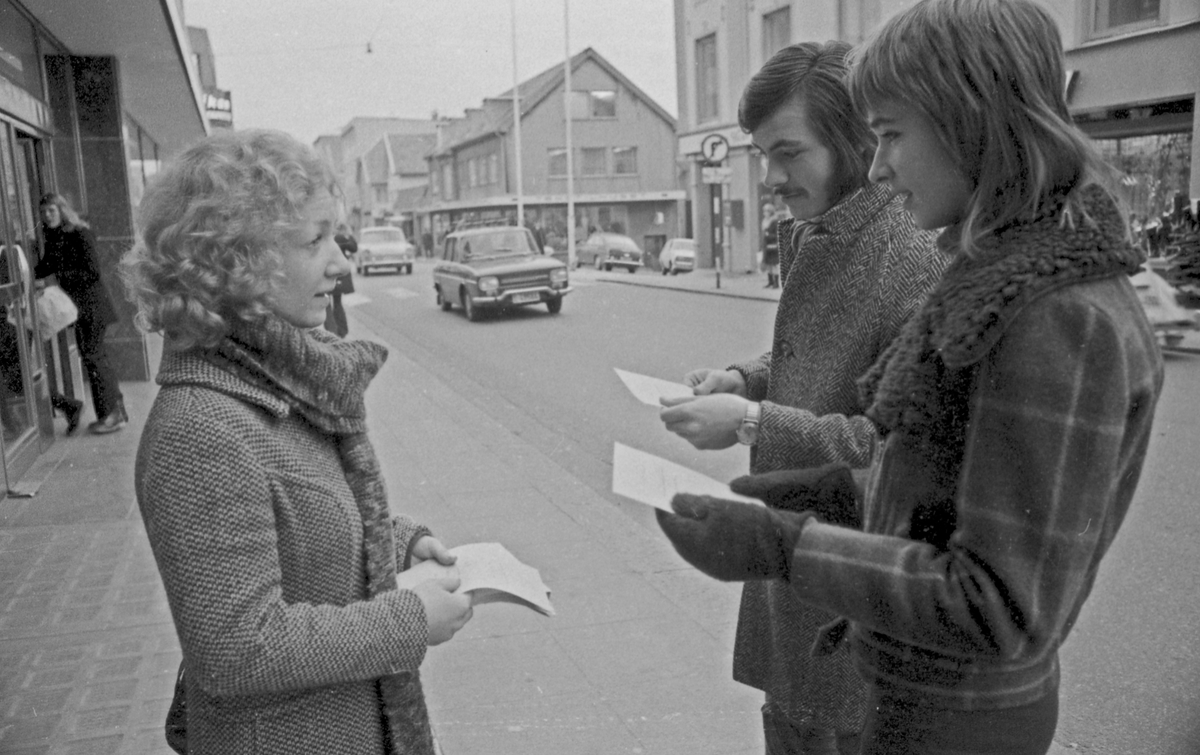 Tre personer, en kvinne og to menn i Haraldsgt. Kvinnen deler ut flygeblad.