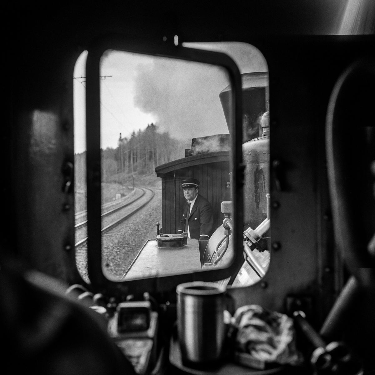 Et vindu i et damplokomotiv. I bakgrunnen står en mannlig frivillig i uniform.