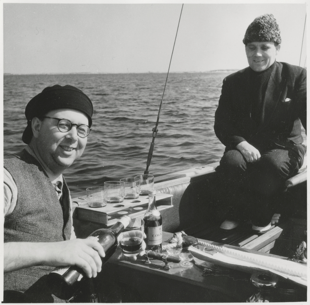 Gösta Åhlén till vänster och Tore Holm till höger i segelbåt med en flaska konjak.