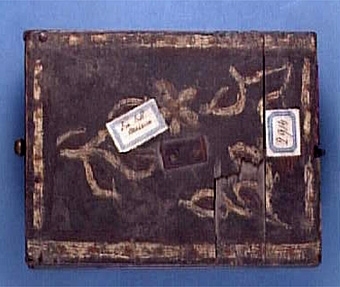 Kassaskrin med utdragbar låda, ena sidans kantlist saknas, lådan låses med fjäderanordning fästad i locket, även lådans sidor målade