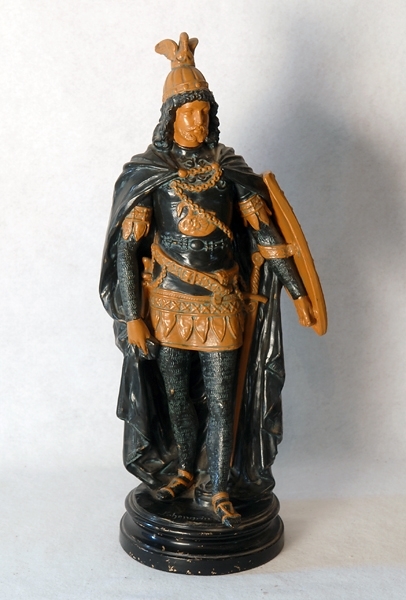 Statyett föreställande Lohengrin i full krigardräkt med slängkappa och sköld. Målad i grönt, svart och gult och stående på svartmålad sockel på vilken namnet "Lohengrin" står skrivet. Se även 73074