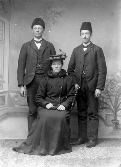 Gruppbild av två herrar och sittande kvinna.