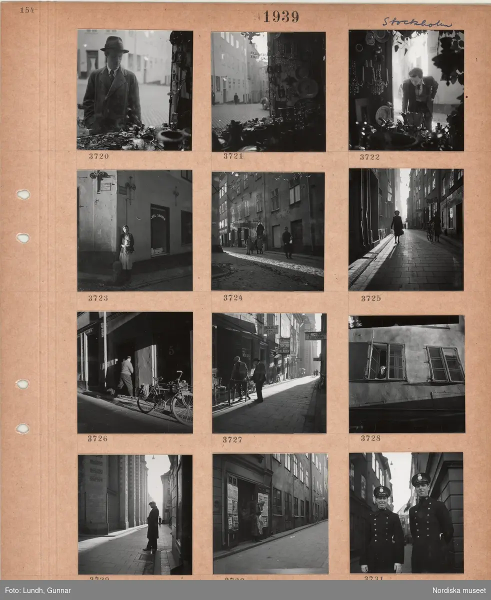 Motiv: Stockholm, en man tittar i ett skyltfönster fullt med saker, en kvinna står i ett gathörn, skyltfönster, barn och en man på en stenlagd gata, äldre hus, butiksskyltar, två kvinnor på en gata, parkerade cykel, en man bär möbler, kvinna tittar ut genom ett fönster, en man står i gränd utanför Storkyrkan, kvinna står vid en port med löpsedlar på dörrarna, två poliser i uniform.