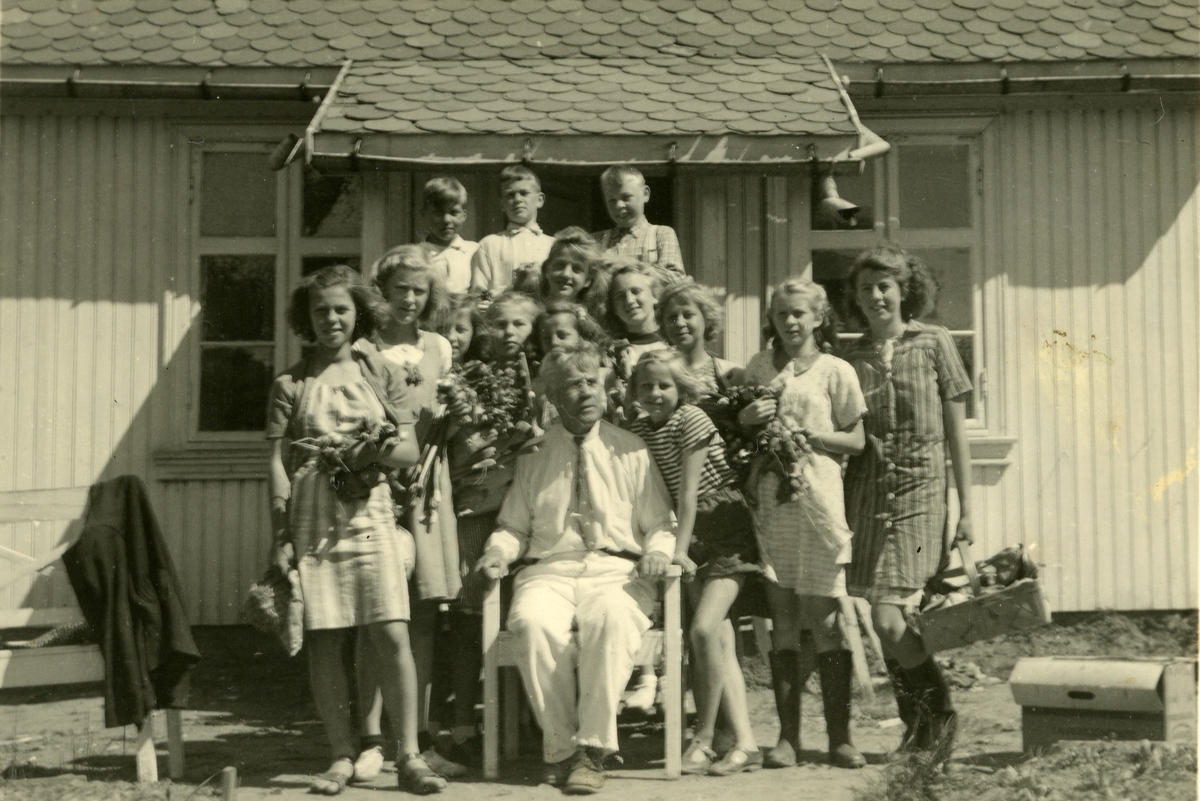 Skoleklasse i Gjøvik skolehage, Gjøvik. Læreren, Ole Haugen Flermoen (1878 - 1956) sitter i midten. Elevene står rundt ham foran inngangspartiet til skolestua.