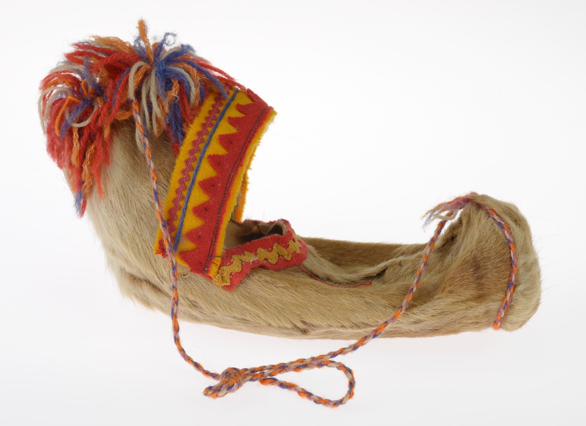 En liten komse med en pute og et dukkehode i. Gjenstandene er undernummerert 01-03. 
FTT.54491.01: En liten komse laget av et uthulet stykke tre som er kledd med garvet reinskinn. På kalesjen er det dekorert med røde pyntebånd av ull festet på et gult bånd av ull. Det er også to flerfargede dusker på kalesjen. i kalesjen er det festet et tvunnet ullbånd som er festet i den andre enden av komsen slik at man kan bære den. Det er også sydd på et pyntebånd i gult og rødt på oversiden.
FTT.54491.02: En liten rød pute sydd av silkestoff som ligger inni komsen.
FTT.54491.03: Et dukkehode laget av plast som ligger i komsen. Håret er støpt og er krøllete. I ansiktet er det malt på øyne og munn. Rundt halsen har dukken et silkebånd.