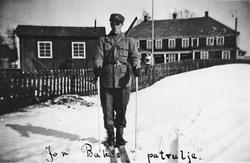 Person, militæruniform, gevær, gjerde, bygninger.