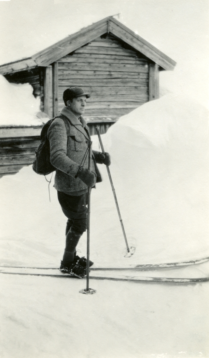 Haakon Garaasen (6/7 1887 - 1957) med ski og ryggsekk i Galåsen (?). Stabbur el. lign. i bakgrunnen