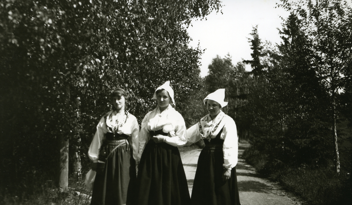 Tre svenske kvinner i bunad gående arm i arm på veien v/ Palmstjernan sommargård v/Siljan, Sverige.