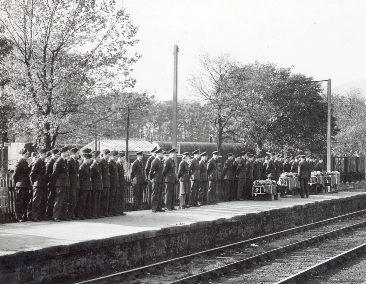 Soldater oppstilt på jernbaneperrong. Bårer til høyre.