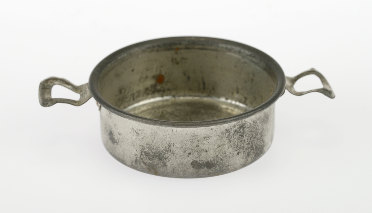 En liten komfyr med tre kasseroller og en steikepanne. Gjenstandene er undernummerert 01-05.
FTT.54454.01: En svartlakkert lekekomfyr som er firkantet med avrundede hjørner. Den er trolig laget av jernblikk og blikk. På kokeflaten er det tre hull for å plassere kasserollene på. Bakerst til venstre er det en 8cm høy pipe. I front er det en sølvfarget blikkdør som er festet med hengsler. På døren er det innskrift og et lite messingfarget og rundt håndtak. Komfyren har buede bein.
FTT.54454.02: En høy kasserolle laget av blikk. I hver side er det loddet på håndtak. 
FTT.54454.03: En lav kasserolle laget av blikk. I hver side er det loddet på håndtak.
FTT.54454.04: En lav kasserolle laget av blikk. Det har vært festet et langt håndtak i den ene siden, men det er nå løs.
FTT.54454.05: En steikepanne laget aav blikk. Håndtaket mangler.