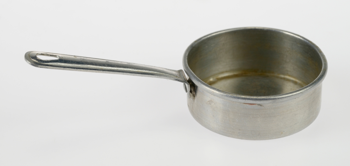 En liten komfyr med tre kasseroller og en steikepanne. Gjenstandene er undernummerert 01-05.
FTT.54454.01: En svartlakkert lekekomfyr som er firkantet med avrundede hjørner. Den er trolig laget av jernblikk og blikk. På kokeflaten er det tre hull for å plassere kasserollene på. Bakerst til venstre er det en 8cm høy pipe. I front er det en sølvfarget blikkdør som er festet med hengsler. På døren er det innskrift og et lite messingfarget og rundt håndtak. Komfyren har buede bein.
FTT.54454.02: En høy kasserolle laget av blikk. I hver side er det loddet på håndtak. 
FTT.54454.03: En lav kasserolle laget av blikk. I hver side er det loddet på håndtak.
FTT.54454.04: En lav kasserolle laget av blikk. Det har vært festet et langt håndtak i den ene siden, men det er nå løs.
FTT.54454.05: En steikepanne laget aav blikk. Håndtaket mangler.