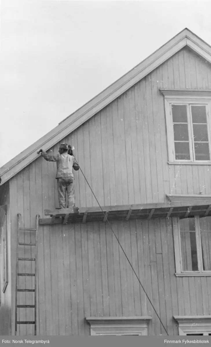 Reprofotografi fra Skjervøy i Troms. Bildet viser en husfasade med en maler som står på et stilas og jobber.