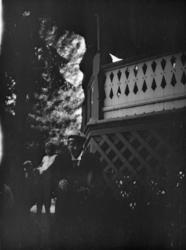 Mann i "sangerlue" og ung jente utenfor stor veranda