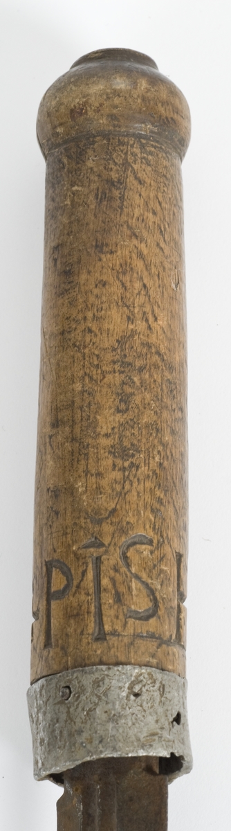 Tregrep med hvitt metall ring nederst. Knappen er formet i treverk..Grepet har innskåret intialer PISH 1824.
Rett tveegget klinge med elipseformet tverrsnitt. To midtstillt smale blodrender.Dekor for enden av blodrendene på begge sider.
