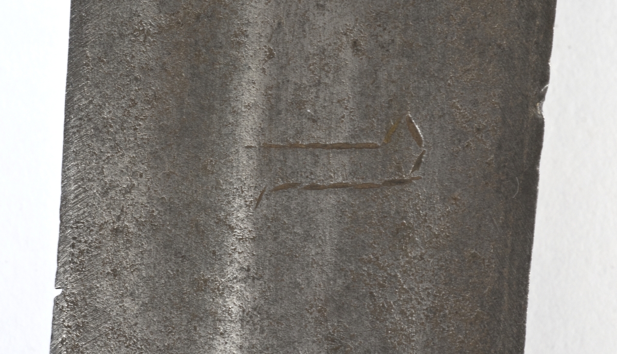 Fasettert rundt knapp med 8 fasetter. Det er innslått 4 smedmerker på knappen, i annethvert felt. Tregrep  Asymerisk åpen parerring med  bøyler med rektangulært tverrsnitt og med kringlefasong med en ytre og en indre parerring. Ytre ring har utsmidde rektangulære partier med kryssfliling. Ytre og indre ring er låst ved at de er tvunnet sammen i senter. Utsiden er smidd som en plateformet deksel. Denne typen pareranordning er trolig norsk
Bred tveegget klinge med 3 brodrender på hver side. Klingen er merket med  Solingens løpende ulv, et hjul og 2 andre symboler på begge sider. Klingen er brukket.