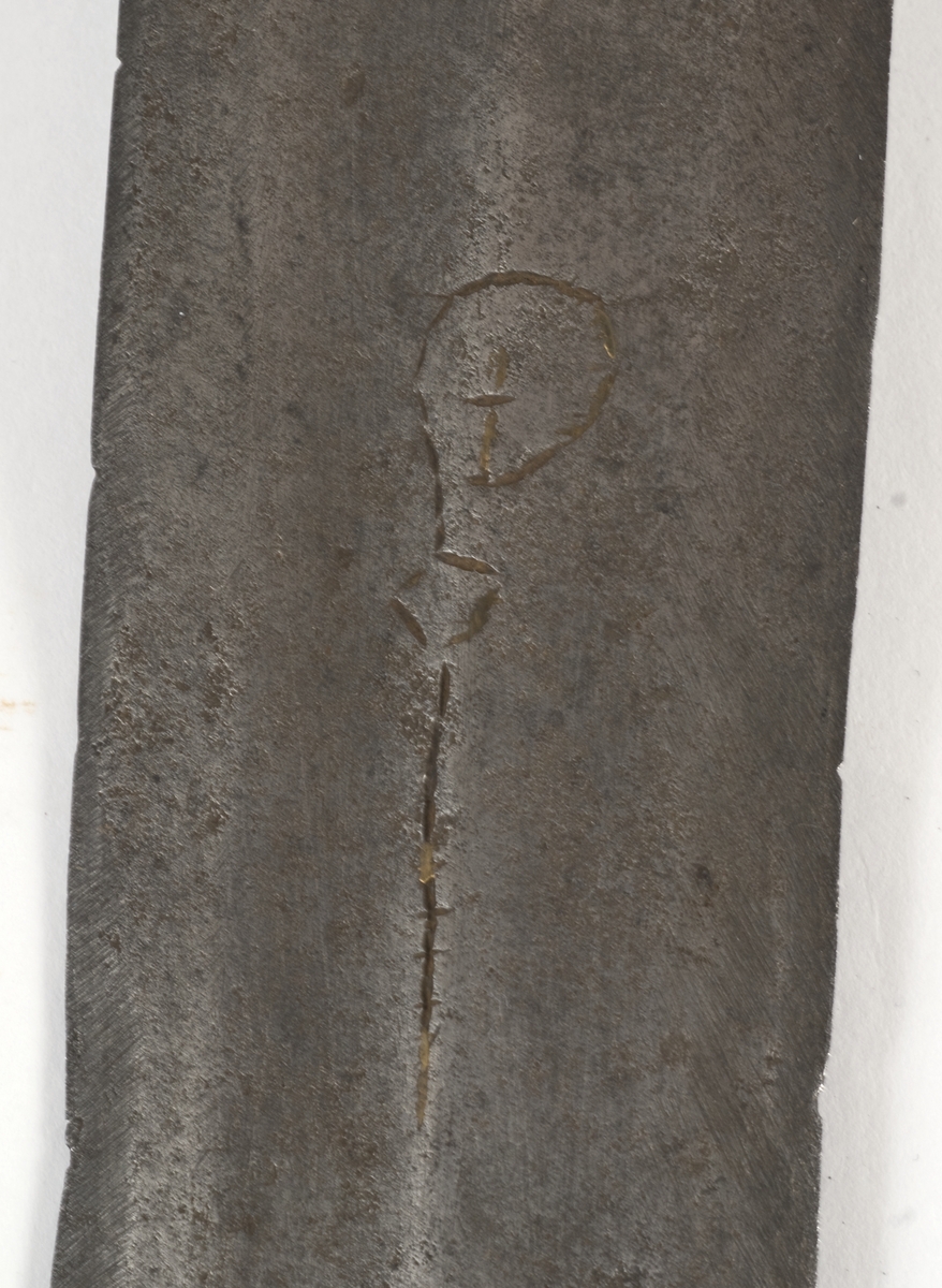 Fasettert rundt knapp med 8 fasetter. Det er innslått 4 smedmerker på knappen, i annethvert felt. Tregrep  Asymerisk åpen parerring med  bøyler med rektangulært tverrsnitt og med kringlefasong med en ytre og en indre parerring. Ytre ring har utsmidde rektangulære partier med kryssfliling. Ytre og indre ring er låst ved at de er tvunnet sammen i senter. Utsiden er smidd som en plateformet deksel. Denne typen pareranordning er trolig norsk
Bred tveegget klinge med 3 brodrender på hver side. Klingen er merket med  Solingens løpende ulv, et hjul og 2 andre symboler på begge sider. Klingen er brukket.