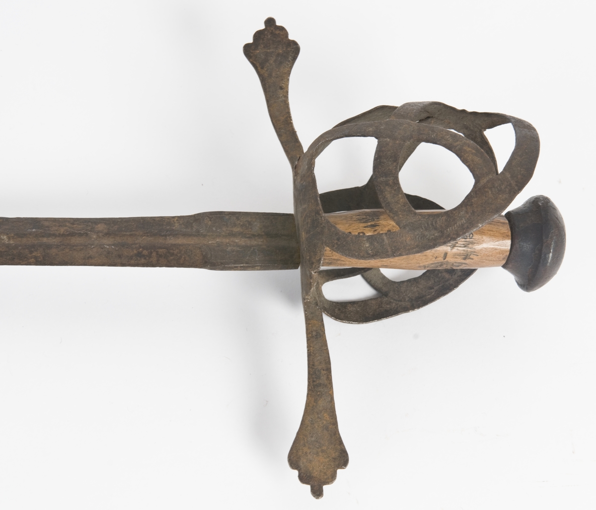 Soppformet knapp  med  strekdekor. Tregrep.  Flate rette  parerstenger som ender i to fliker. Festet har rester av dekor.
Symetrisk kurvfeste med tombøyle og nyreformede parerplater.  
Elipseformet rett  klinge med kort blodrand på øvre del. Klingebryst har dekor.
Trebalg trukket med lær og sydd på innsiden.