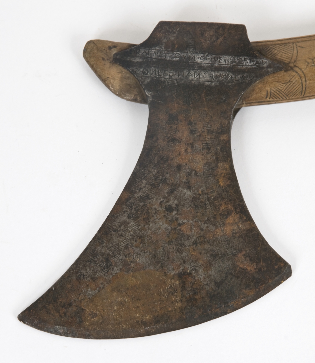 Asymmetrisk blad med lang øvre spiss og kortere nedre spiss. Bladet er klieformet. med påsmidd egg- Øksen har stset dekor på begge sider. Skjellmønstet smedmerke på utsiden. Øksen er datert 1689.
Øksehammeren har skaftehull og fliker.
Gammelt skaft med dølle,pigg.og 2 oppsmidde fliker.
Skaftet er krummet og merket med navn og datert 1688. Skftet er noe avkortet.