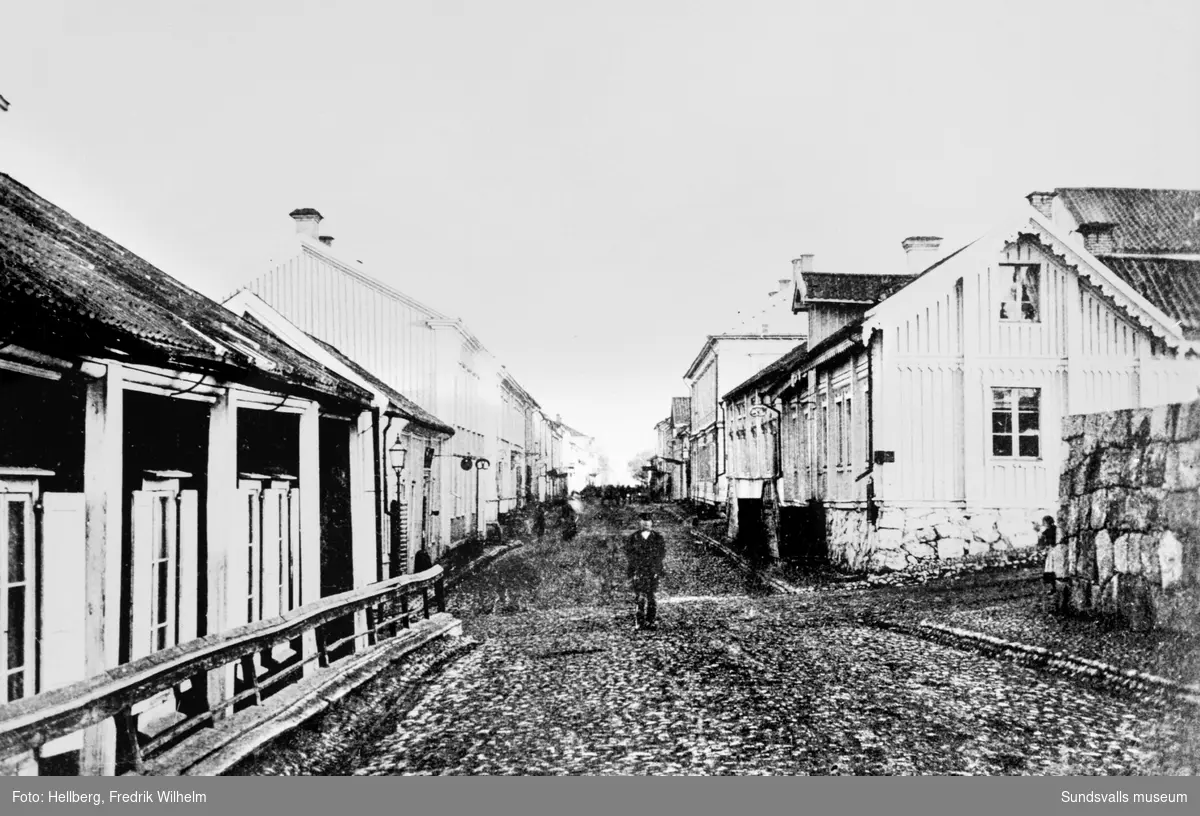 Sundsvalls stadskärna före branden 1888. Storgatan österut från Badhusgränd/Stora Nygatan, till höger FW Hellbergs bageri och fotoateljé som brann 1878. Kyrkomuren ses närmast till höger.