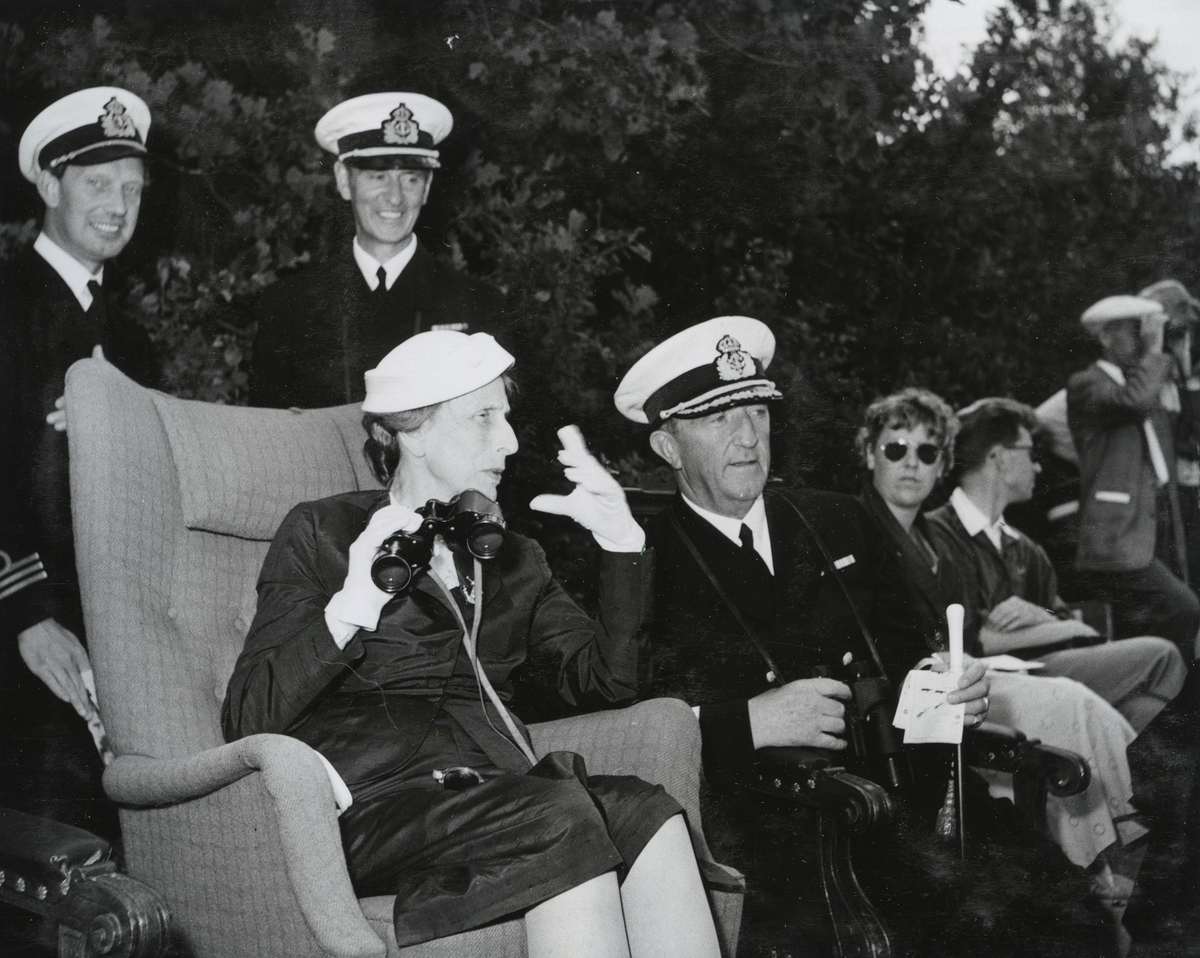 Drottning Louise sitter i en fåtölj med en kikare i högra handen i samband med "Operation Kullen" 1955. Hon konverserar med konteramiral Samuelson som sitter på hennes vänstra sida. Bakom amiralen står kommendörkapten Bengt Lind af Hageby och en kapten. I bakgrunden till höger ytterligare civilklädda personer.