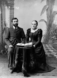 Portrett av ektepar. Mann og kvinne sittende ved et rundt bo