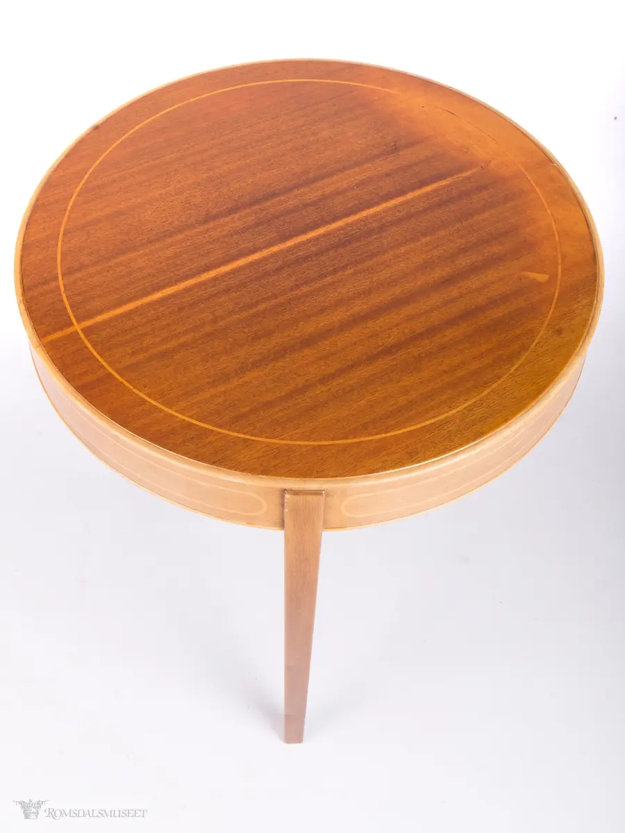 Lavt bord med rund bordplate og rette ben. Finer er satt inn i bordplate og sarg.
