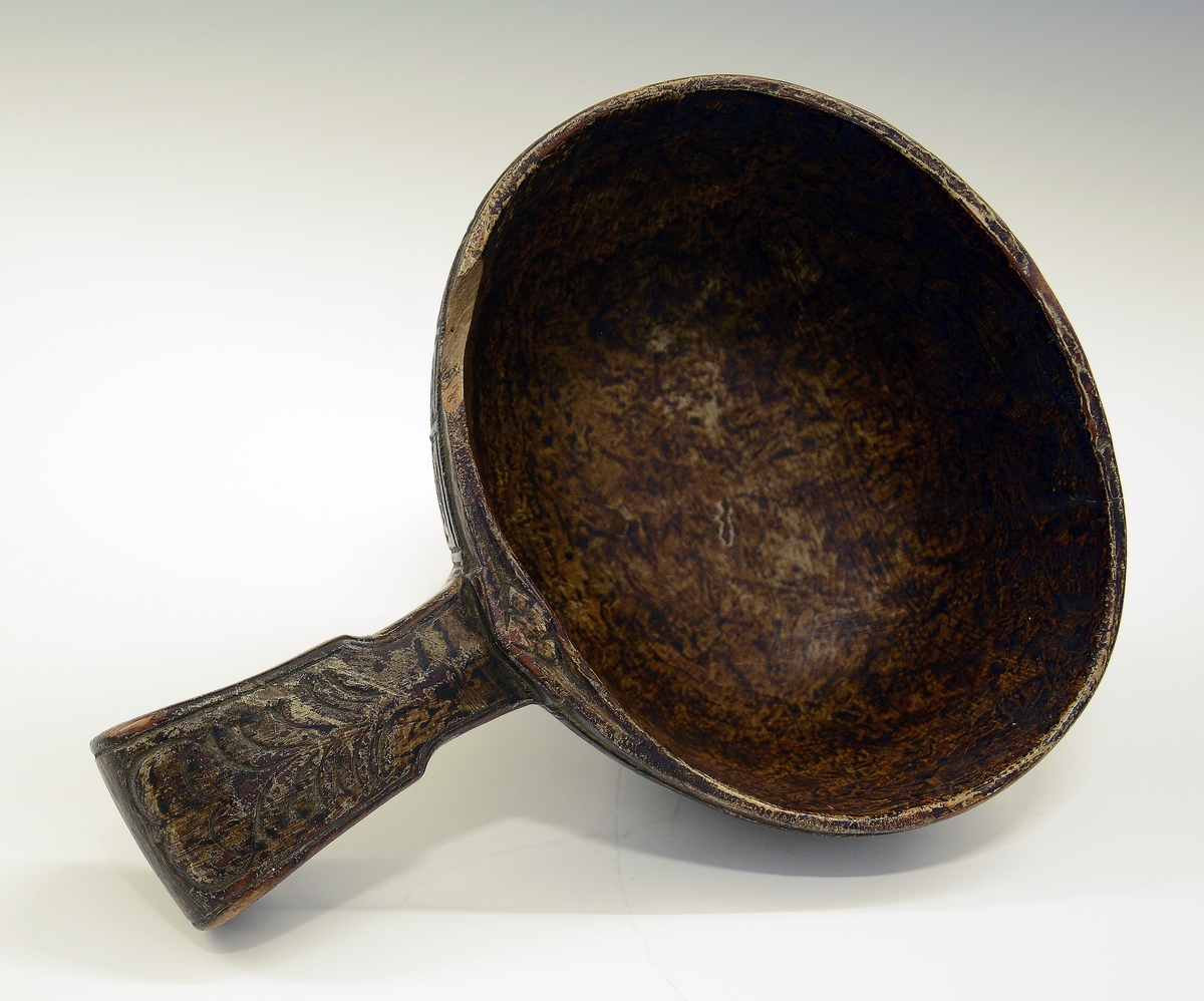 Øløse i tre. Fra protokollen: Øse fra 1806. Under bunden skaaret JTS 1806. Bladorn. paa skaftet. Utenpaa baand av kerbsnitruter, indelt i 4 kanter. Rundt kanten oppe, nede og 5 paa tvers og ett dobbelt ved skaftet.