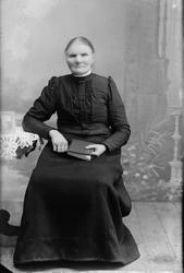 Portrett, helfigur. Ukjent kvinne sittende ved bord.