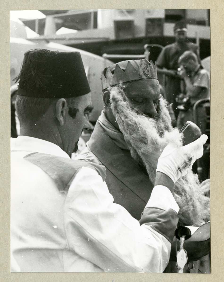 Bilden föreställer två män ombord på minfartyget Älvsnabben, båda i utklädnader. Den ena mannen är utklädd till Kung Neptun med en krona och ett stort skägg. Bilden är tagen i samband med ett linjedop under fatygets långresa 1966-1967.