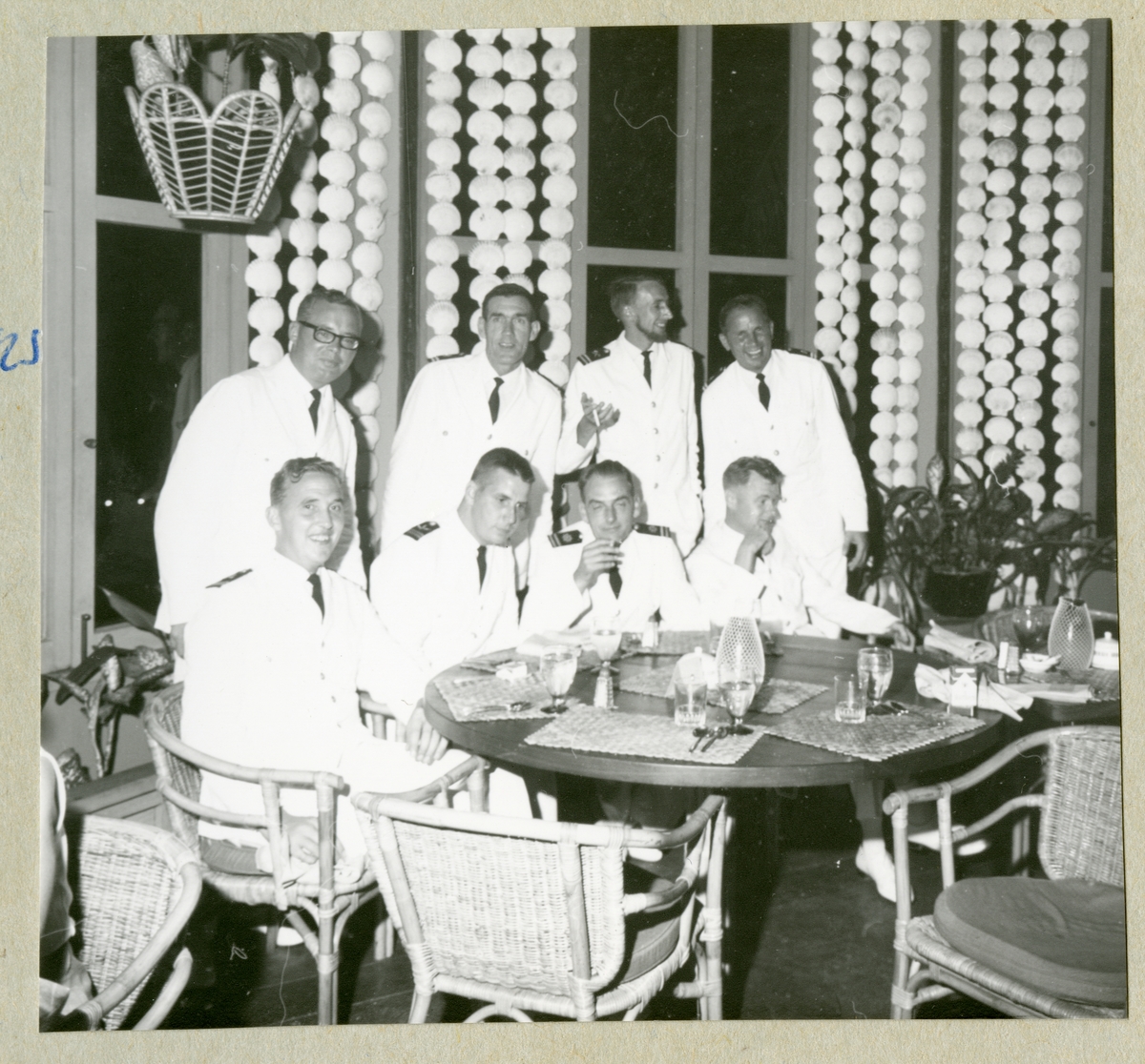Bilden föreställer besättningsmän i vita uniformer som poserar för en gruppbild i samband med ett restaurantbesök. Bilden är tagen under minfartyget Älvsnabbens långresa 1966-1967.