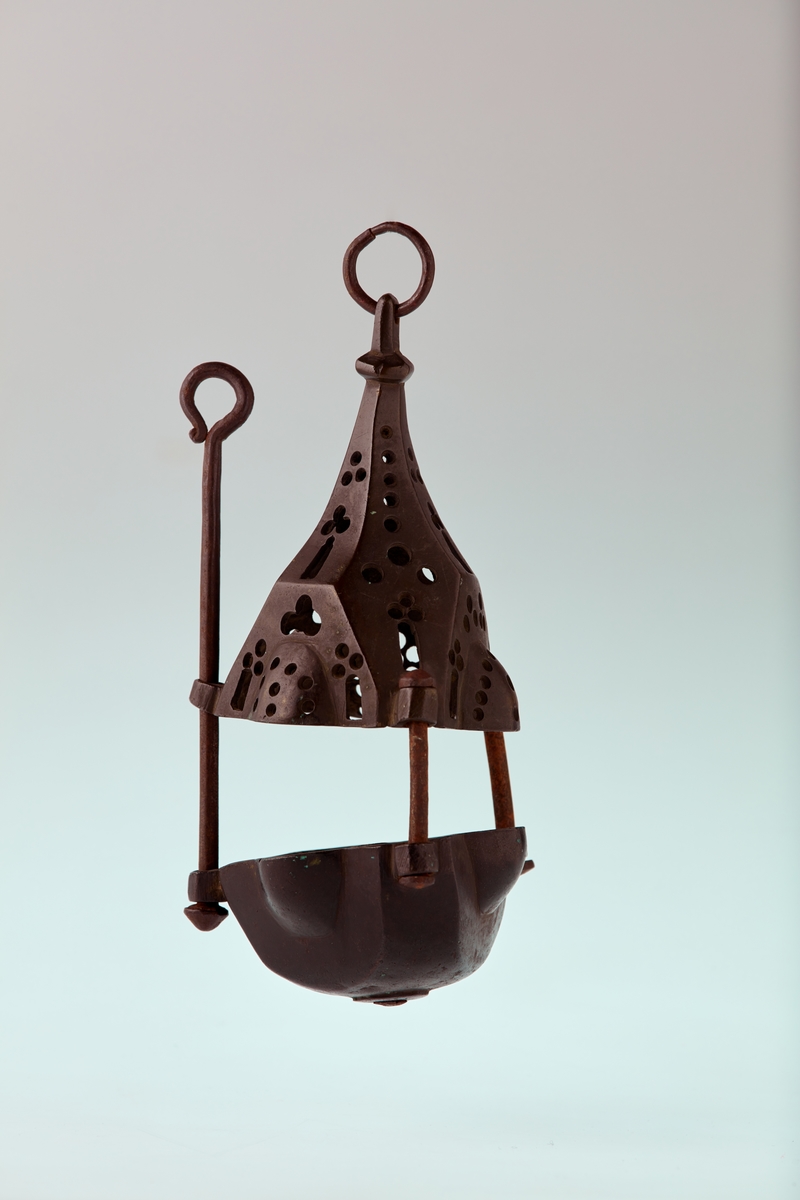 Bronse. 6 sidet. 3 av sidene med kuleformet utvidelse. Skål med pipe i centrum. Firpassformen viser hen på slutten av middelalderen. Den skjematiske og grove utførelse tyder på hjemlig produksjon. Ligger nær å gjette på Tunsberg. Etter reformasjonen er en lysepipe satt inn. Mulig denne lysestake har hengt etter en snor og likeledes den lange glidestangen