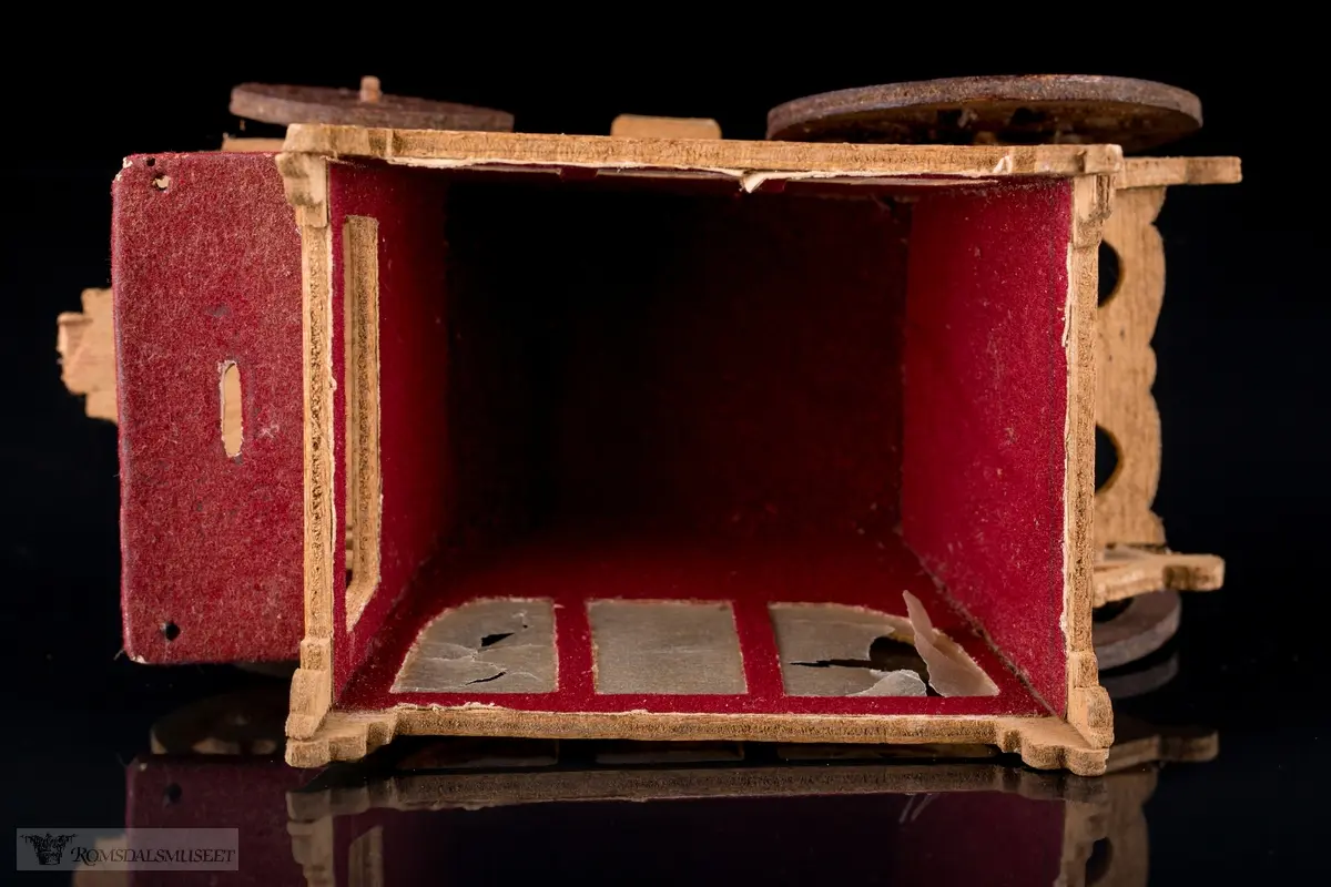 En liten leke- hestevogn i kryssfiner. To store og to små hjul, kledd med rød filt og vokspapir er brukt som vinduer.