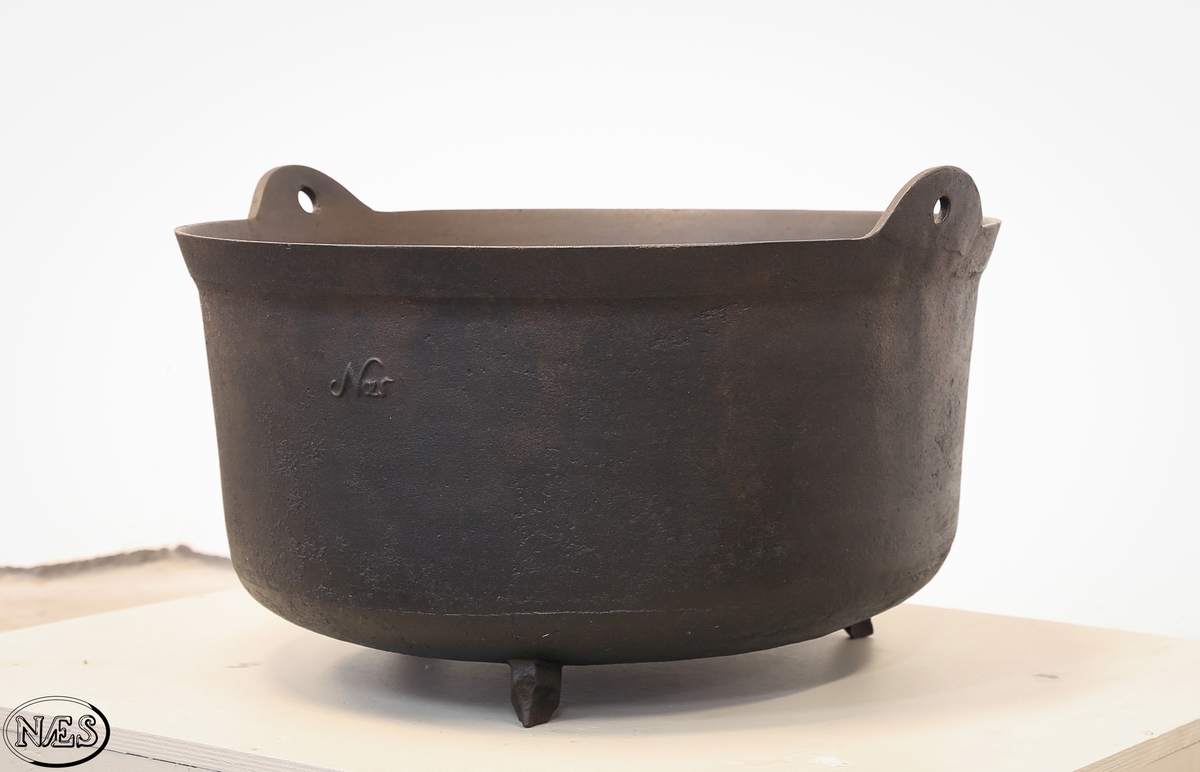 Rund jerngryte med tre bein og to ører på øvre kant for feste av hank.