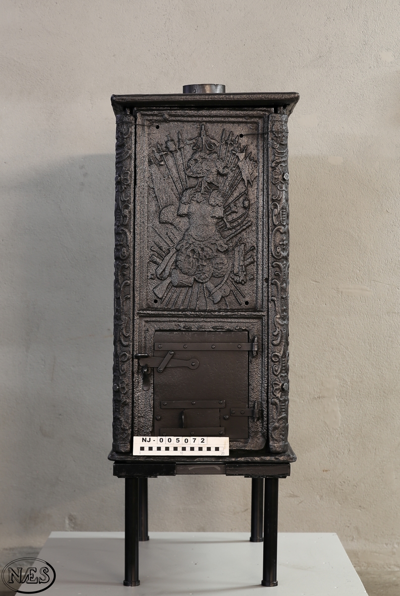 Kasseovn med ovnsdør på kortsiden og røykuttak i topplaten. Ovnen har løse skinner med bruskornamenter. På langsidene er Gyldenløves våpen omgitt av krigerske emblemer med innskrift i knekket bånd over. Øverst står det innskrevet ANNO og nederst på platen 1687. På kortsiden er det øverst krigerske emblemer og nederst den norske løve omkranset av brusk-kartusj.