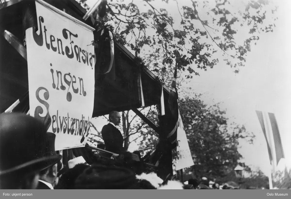 talerstol, mann, tale, plakat: "Uten forsvar ingen Selvstændighet", flagg, banner