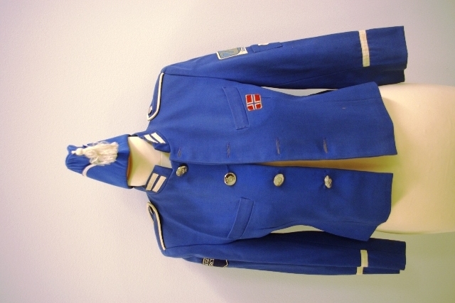 Jakke (a) med blå knapper med lyremotiv.
Hvite striper nederst på hvert erme, to små striper på hver side av halskanten, skulderklaffene er kantet med hvite bånd og kneppet på en knapp med lyremotiv.
Tøymerker på jakken som alle er påsydd for hånd: det norske flagg, Gjøvik Byvåpen, tøymerke med brodert lyre, Mjøsegnenes kretsmerke: avrundet i formen med en spiss ned på midten
Buksa (b) har stikklomme. Den har blå og hvit dekor, hvit stripe påsydd på yttersiden av hvert bukseben som er svakt innskrånende.