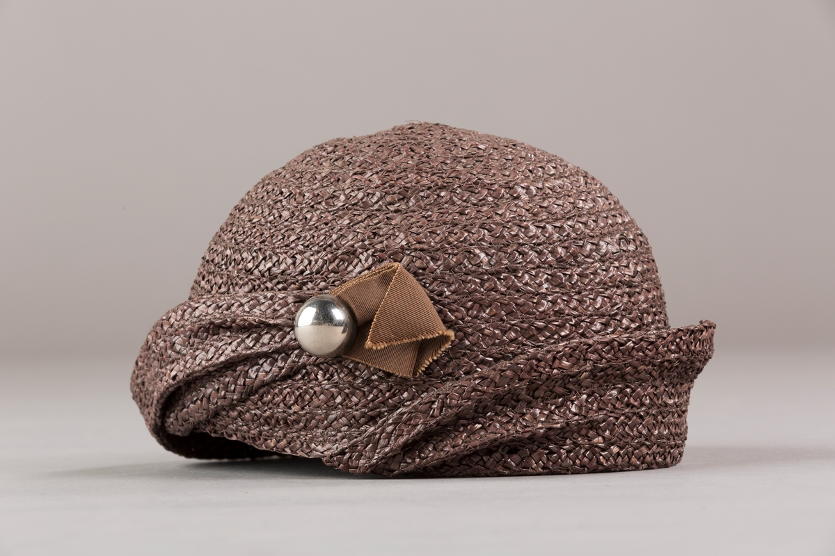 Form: Sirkelformet, avrundet  med brem og lita silkesløyfe med knapp. Bomullsbånd innvendig
Brem oppbrettet i spiralform med bredde økende til avslutning hvor den er festet til pullen med en plastknapp og sløyfe