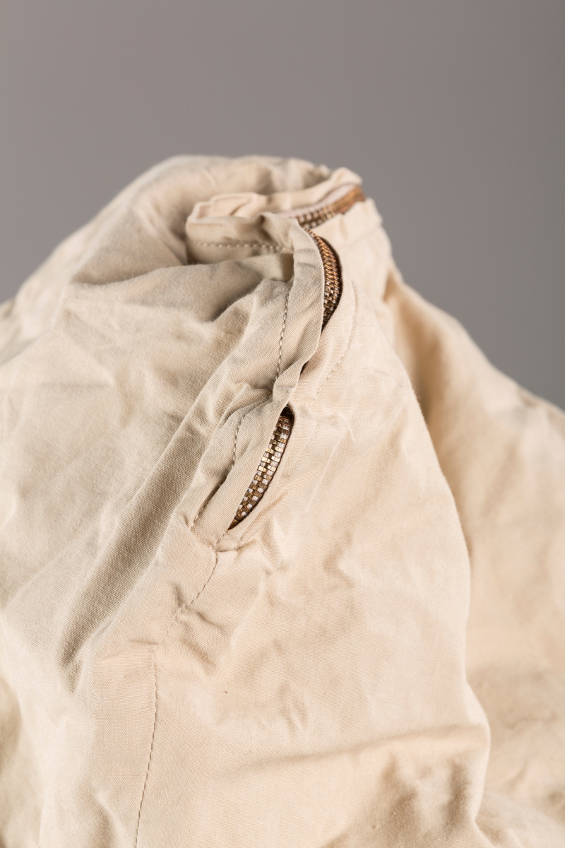 Form: Vanlig anorakkfasong med strikk i livet. 2 brystlommer med knapp.
Hette med glidelås på topp midt, snøring.
Glidelås helt ned foran.
Innermansjett med strikk i ermene.