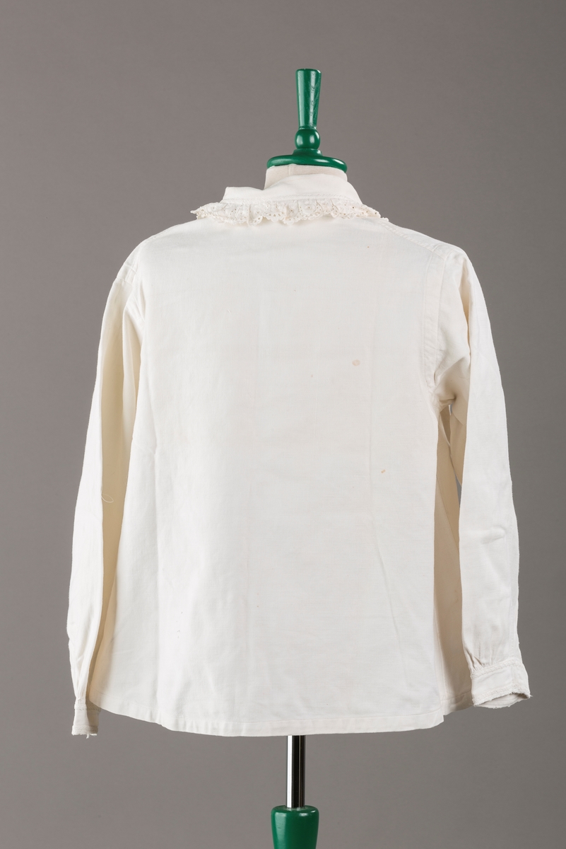 Form: Hoftelang trøye, Lange ermer, krage. Kragen og åpningen foran er kantet med  maskinprodusert blonde. Tre biser på hver side av åpn. foran. Lukkes med to løse knapper.