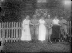 3 kvinner, 3 menn i uniform foran hus med gjerde