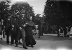 Mann og kvinne går arm i arm, finkledt i park.